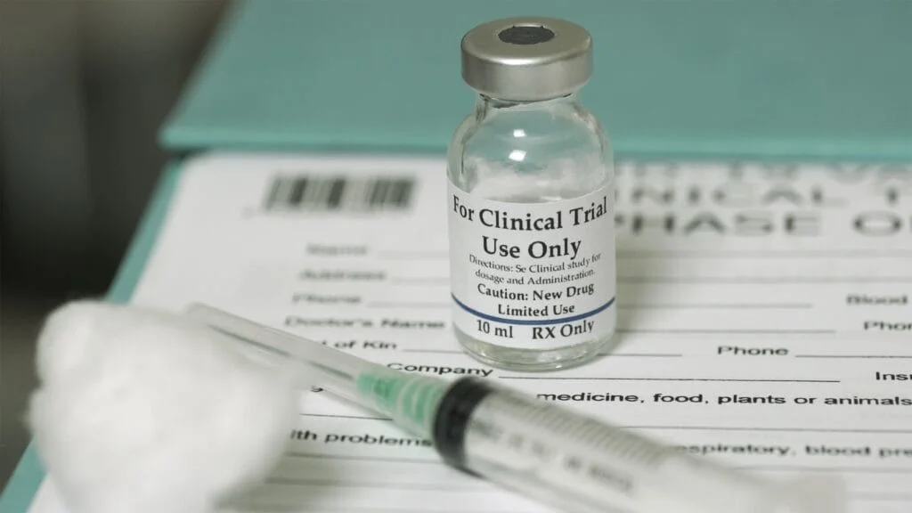 Photo showing a vial and syringe. Vial has label reading "for clinical trial use only"