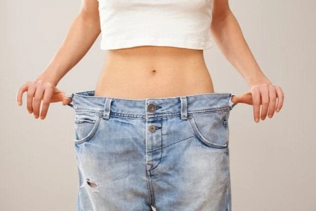A slender woman pulling out the oversized waistband of her jeans, visually demonstrating significant weight loss. Photo is for the blog post The Cellular Reset Triad: Optimizing Your Metabolic Engine