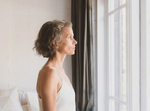 middle-aged woman looking out a window for the blog post on managing disordered eating patterns during the menopause transition