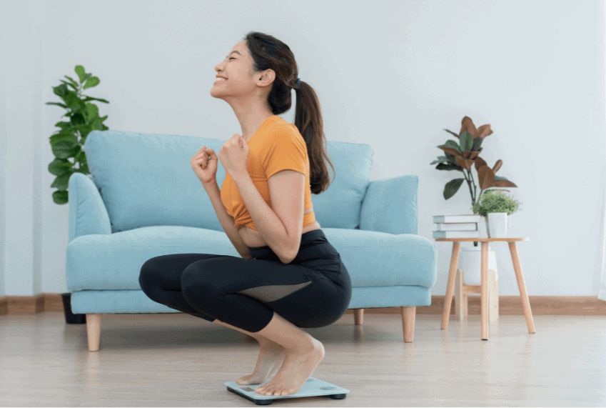 A woman is crouched on a scale celebrating her weight loss.