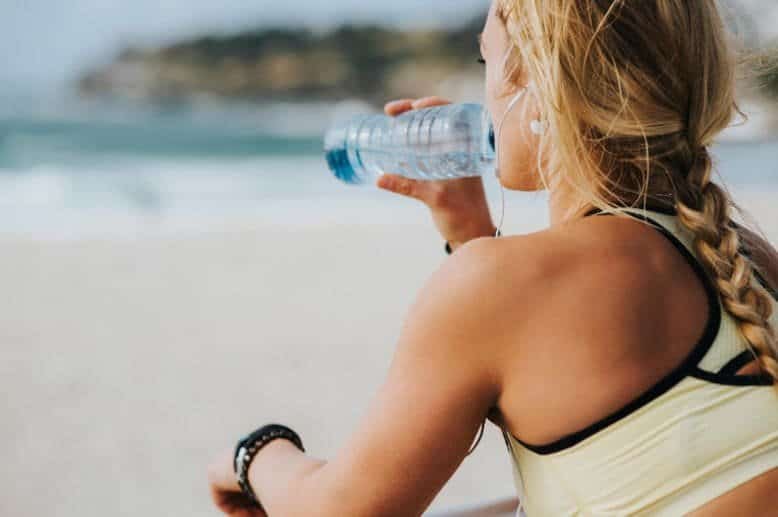 A woman sitting on the beach drinking water.