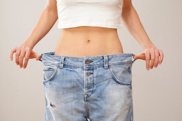 A slender woman pulling out the oversized waistband of her jeans, visually demonstrating significant weight loss. Photo is for the blog post The Cellular Reset Triad: Optimizing Your Metabolic Engine