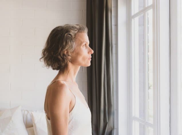 middle-aged woman looking out a window for the blog post on managing disordered eating patterns during the menopause transition